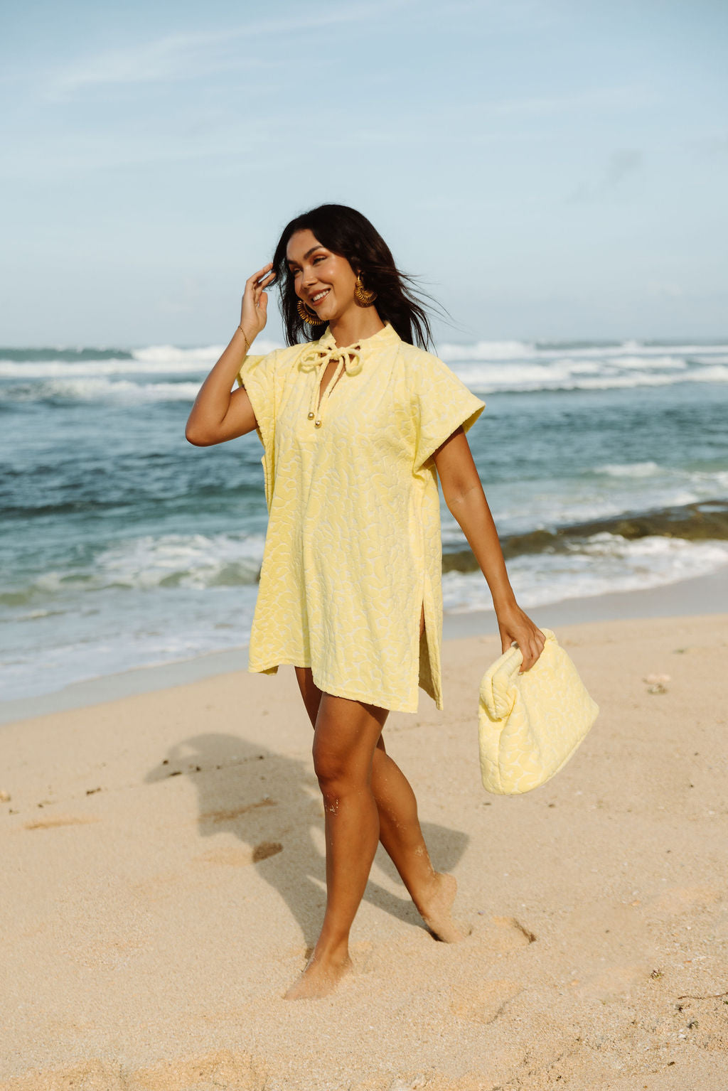 The Mila Poncho in Butter Yellow, walking the shoreline.