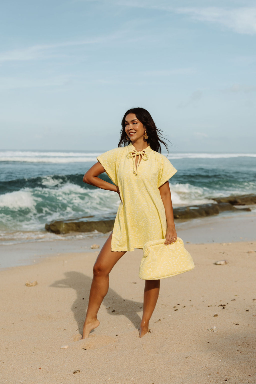 The Mila Poncho in Butter Yellow, full length against the surf.